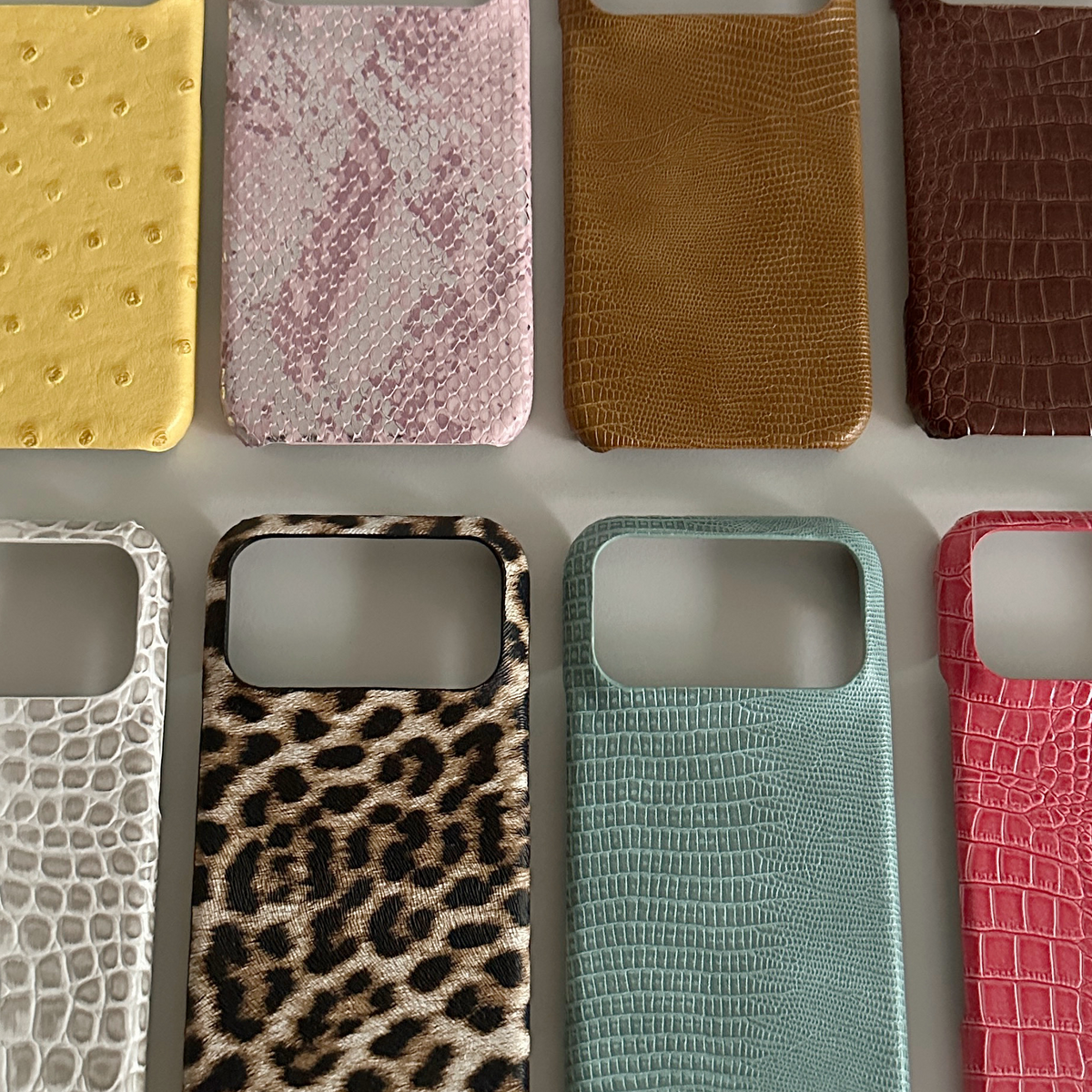Yellow ostrich, pink snake, tan and brown crocodile phone cases above leopard and teal cases with camera openings