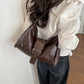 Brown soft vegan leather hobo bag with front buckle strap worn on the shoulder, seen from behind with a white blouse