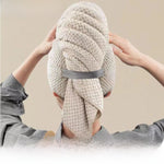 Woman wrapping her hair in a beige pineapple plaid hair towel secured with a grey elastic strap, back view