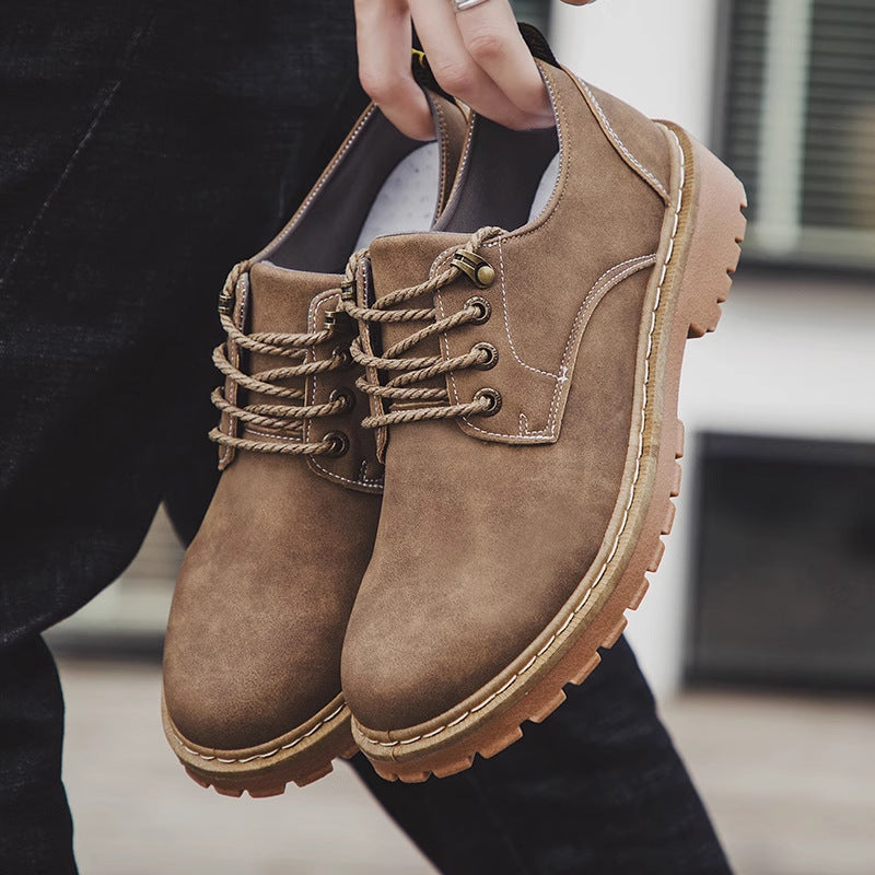 Pair of khaki low-top lace-up derby shoes with a lugged rubber sole held in one hand over dark trousers