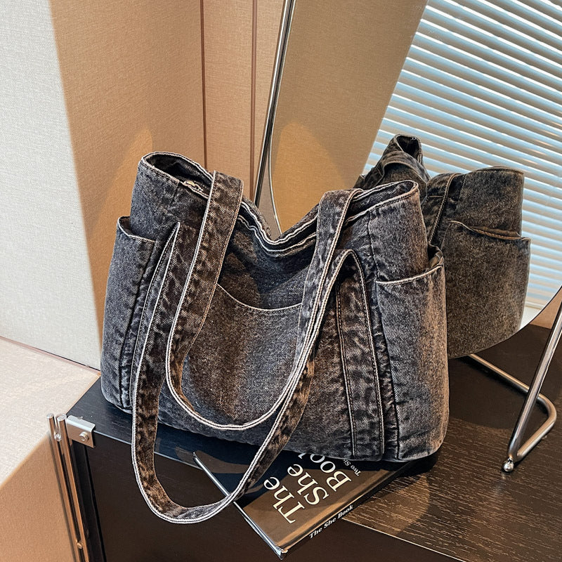 Pair of washed dark brown denim shoulder totes with end patch pockets and contrast topstitching on a cabinet