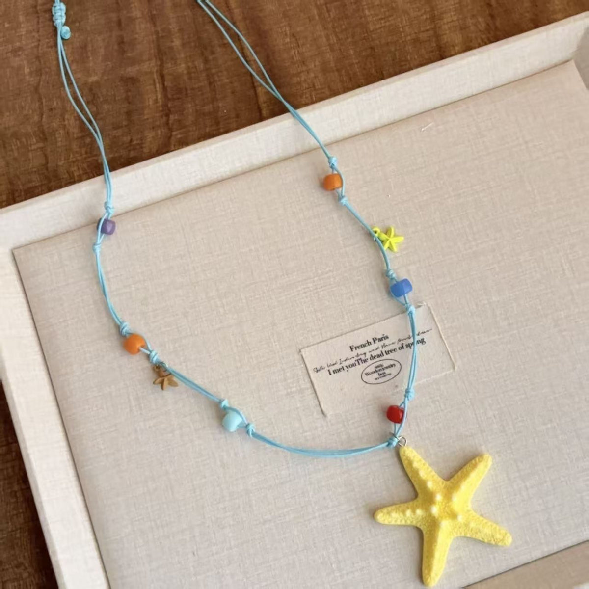 Yellow resin starfish cord necklace with colored beads laid in a gift box with adjustable blue cord