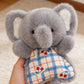 Grey plush elephant squishy bean bag toy in hand, big ears and a blue check cotton apron
