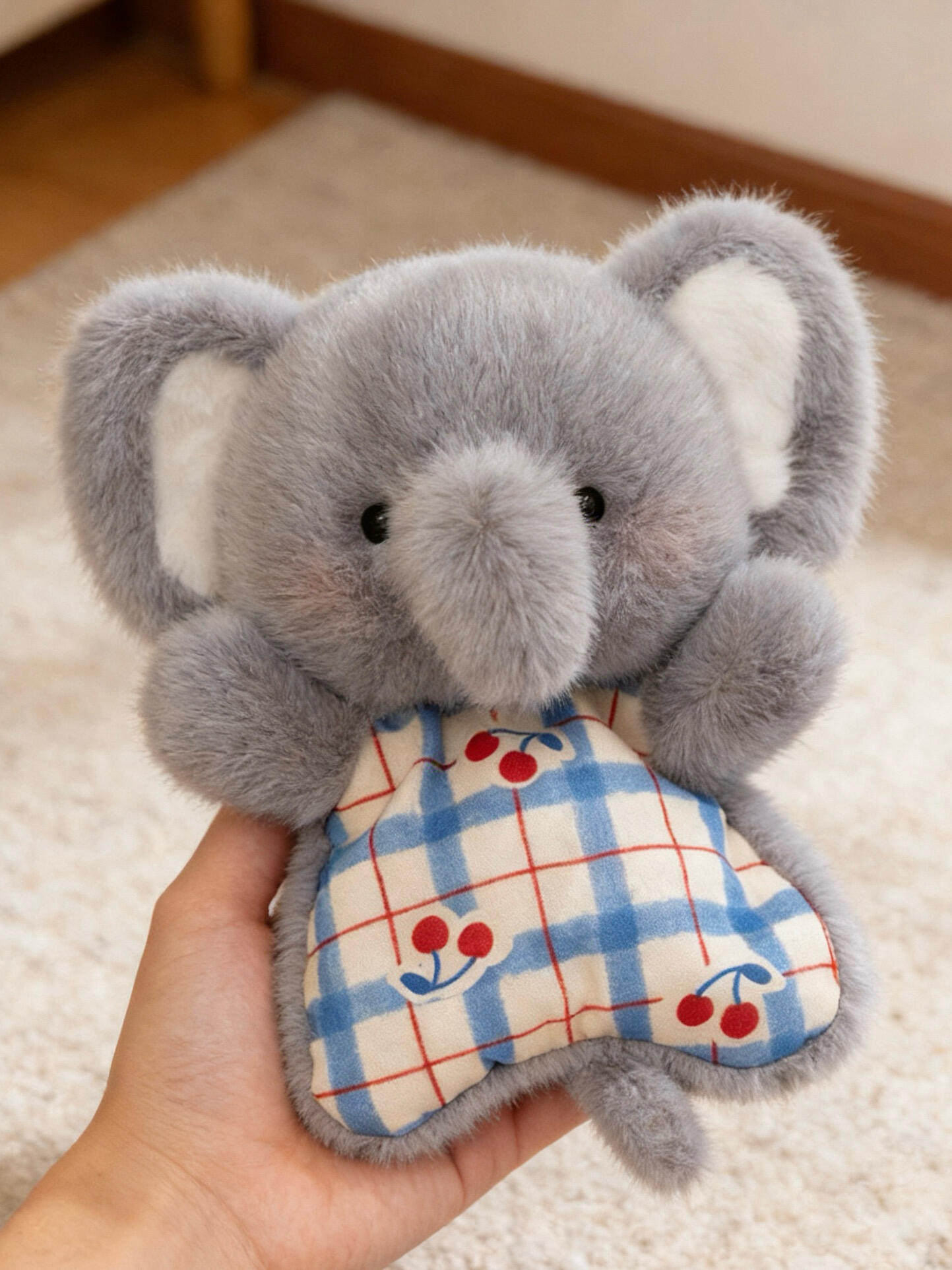 Grey plush elephant squishy bean bag toy in hand, big ears and a blue check cotton apron