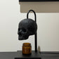 Skull candle warmer lamp on a round metal base warming a scented jar candle