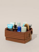 Brown ribbed stripe makeup organizer open and filled with bottles, jars, a brush and a razor