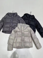 Grey, black and off white hooded down puffer jackets laid flat on hangers showing box quilting