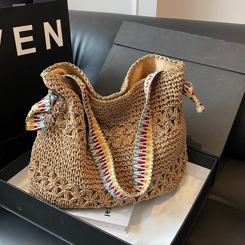 Khaki woven straw shoulder tote with colorful boho strap resting in a gift box