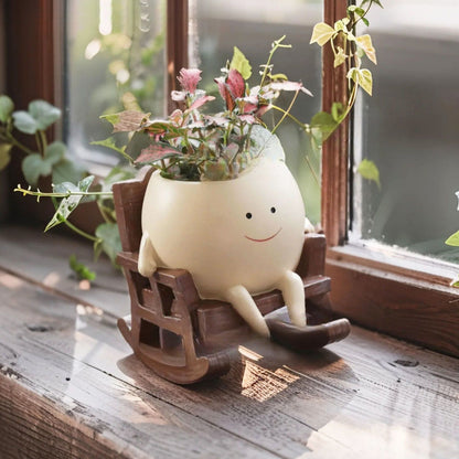 Cream smiling face resin planter in a brown rocking chair with a small plant on a windowsill