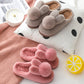 Taupe brown and burgundy plush bunny slippers with pom pom tails on a polka dot cushion beside a clock and knit throw