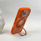 Orange phone case leaning on its folded-out ring stand in portrait position, camera surround at the top