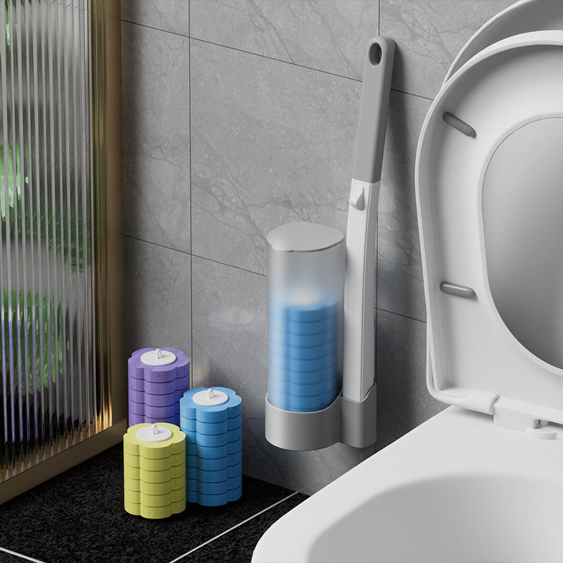 Gray toilet brush handle standing in a wall mounted holder beside a toilet, with purple, blue and yellow sponge heads