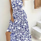 Blue and white floral halter neck sleeveless tiered swing maxi dress shown from the side by a staircase