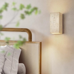 Yellow travertine LED wall sconce glowing warm on a bedroom wall beside a rattan headboard
