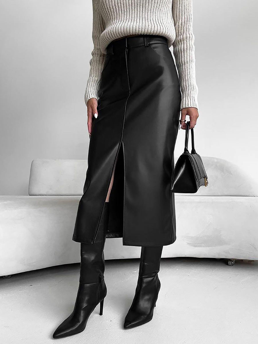 Woman in a black PU leather midi skirt with a front slit, cream sweater, black boots and a black handbag
