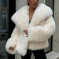 Woman in a cream vegan fur jacket with a wide collar and fluffy sleeves over black trousers on a street