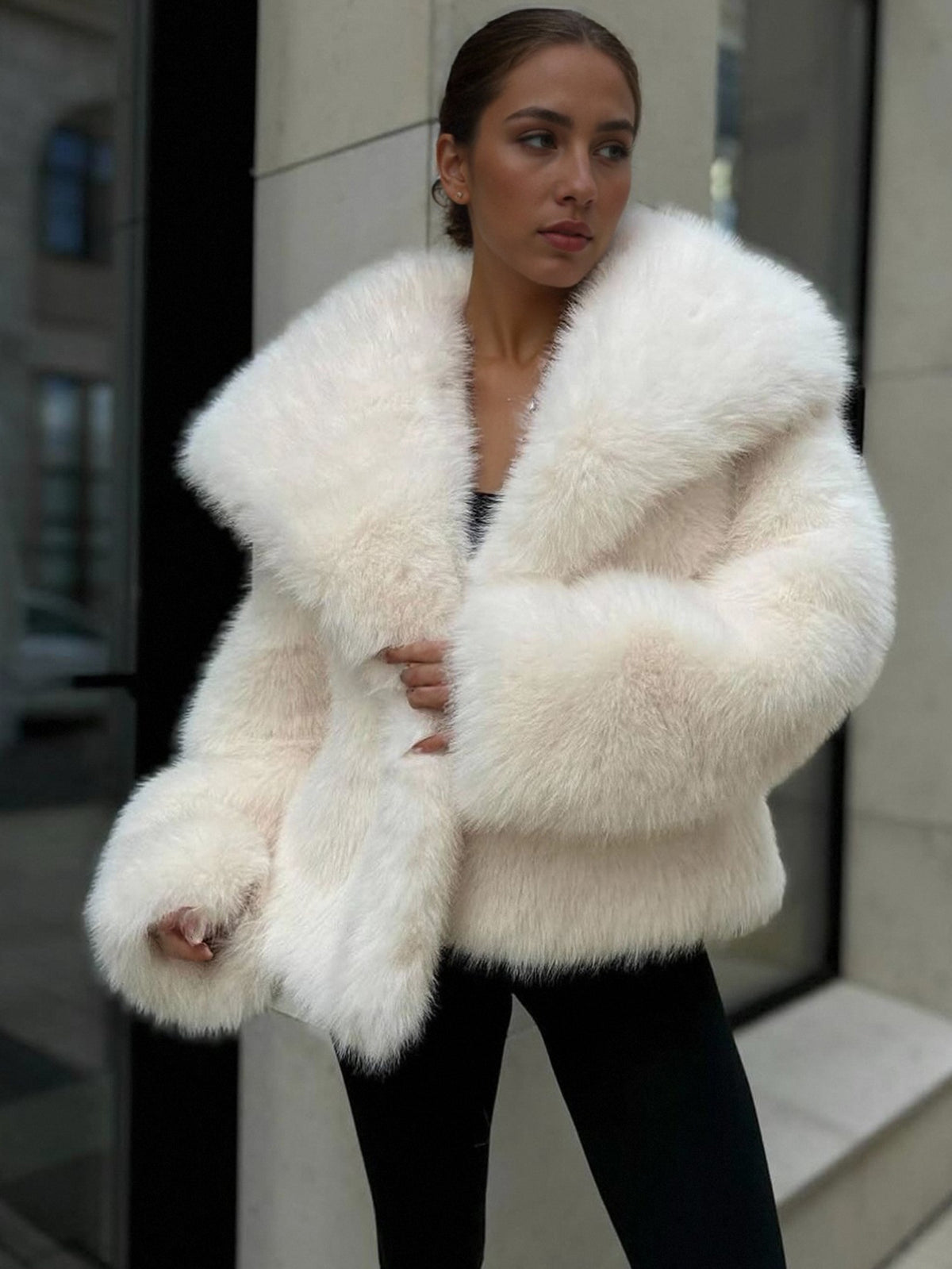 Woman in a cream vegan fur jacket with a wide collar and fluffy sleeves over black trousers on a street