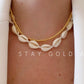 Cowrie shell choker on cream cord worn with a separate gold bead chain layered above it