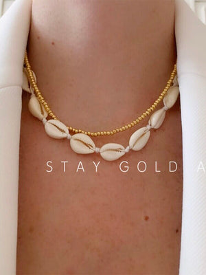 Cowrie shell choker on cream cord worn with a separate gold bead chain layered above it