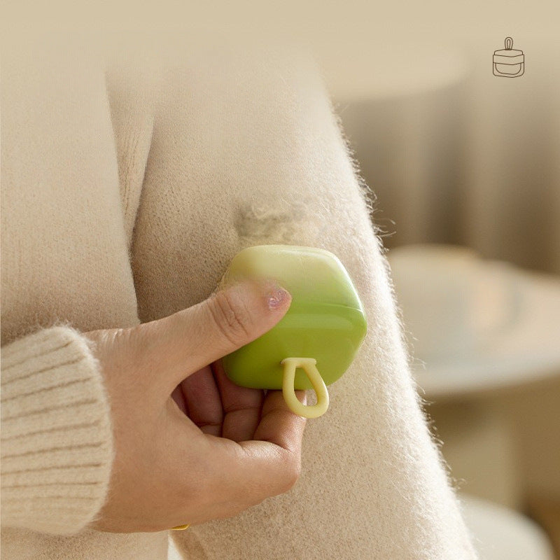 Green silicone lint remover held against a cream knitted jumper over a patch of loose fluff