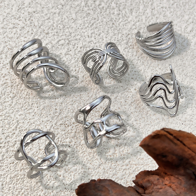 Six open silver tone steel rings of wire lines laid on a pale textured stone beside a piece of bark