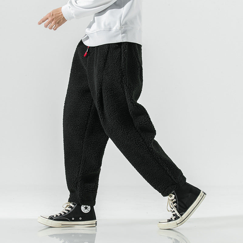 Black plush harem pants in a walking stride, side view showing the loose cut and tapered ankle