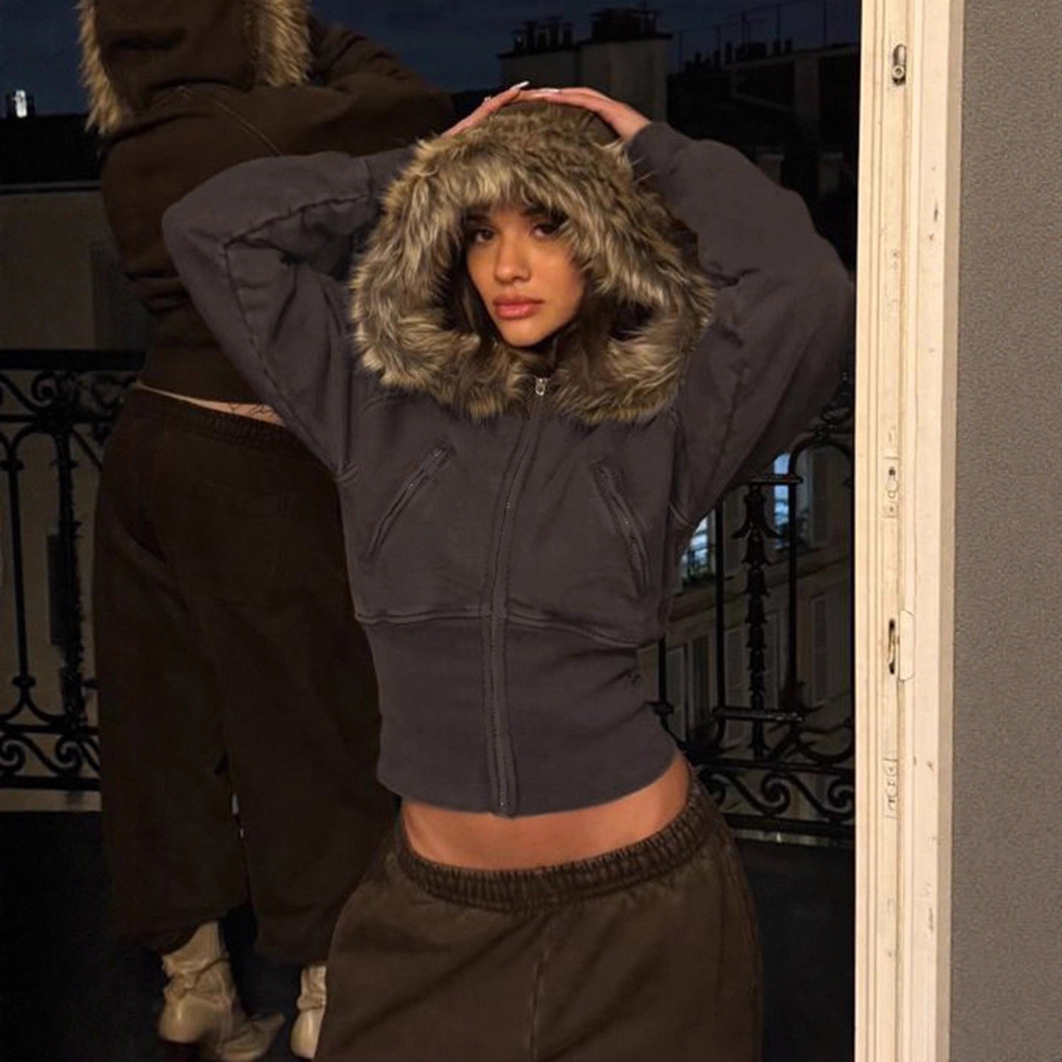 Model on a balcony in the charcoal cropped fur trimmed hooded zip jacket with a plush fur hood up