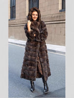 Woman in a long brown vegan fur coat with the hood up, hand at her chin, on a city street