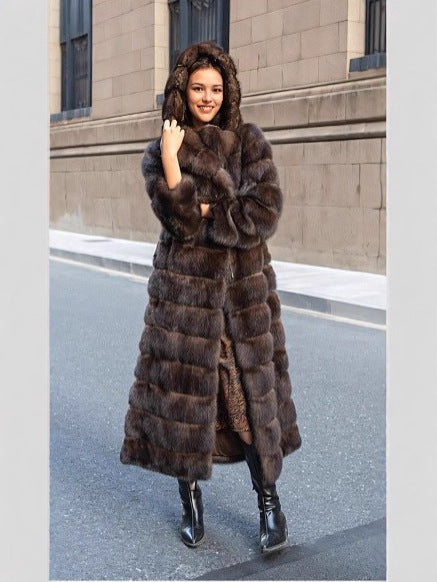 Woman in a long brown vegan fur coat with the hood up, hand at her chin, on a city street