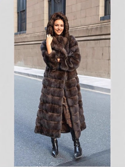 Woman in a long brown vegan fur coat with the hood up, hand at her chin, on a city street