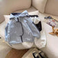 Light blue boys hooded jacket laid beside light gray sweatpants on a cream sofa