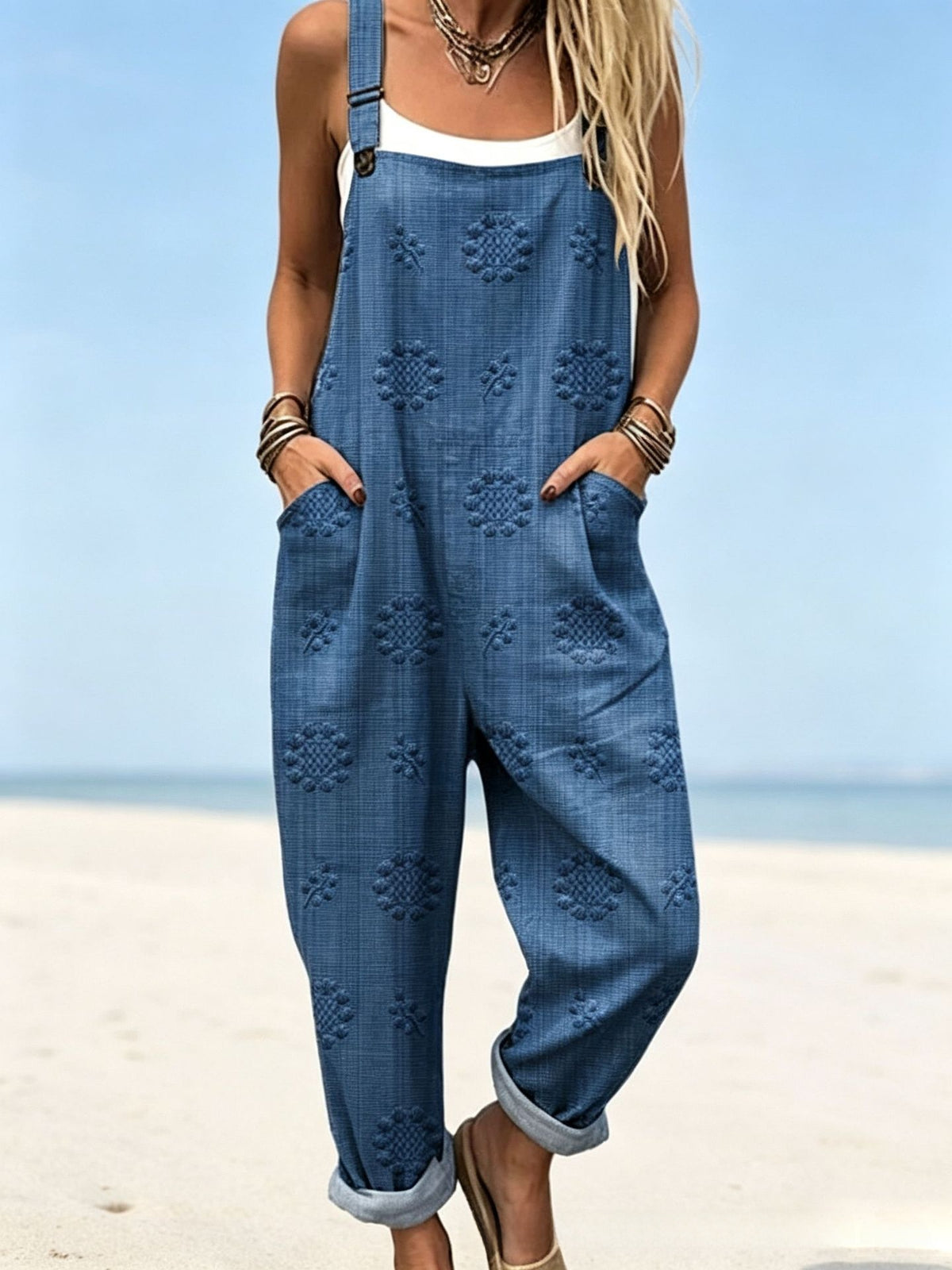 Size 3XL option: Denim blue overalls with an embossed flower texture, cuffed legs and pockets on a beach