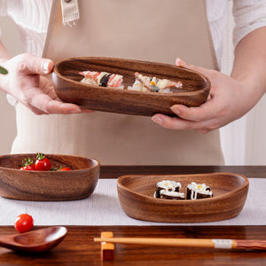 Hands holding a walnut tone boat bowl of sushi over a set table with chopsticks