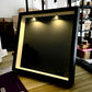 Black shadow box leaning on a table with two small spotlights lit at the top and a dark empty backdrop