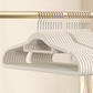 Off-white flocked hangers in a row on a rail, close view of the slim shoulder shape