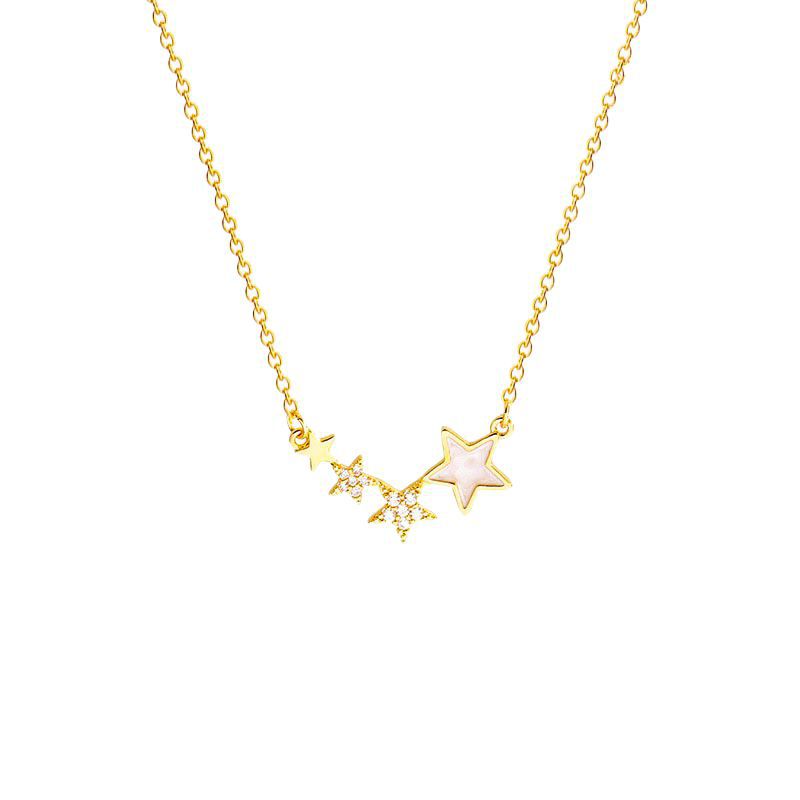 Gold and silver star necklaces draped on a cream plate near a candle