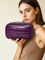 Woman holding a purple crocodile pattern leather cosmetic bag against her shoulder