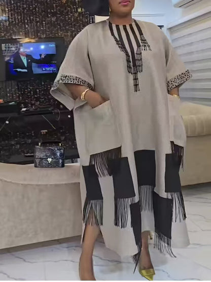 Apricot polyester boubou kaftan dress with beaded tassel neckline and black fringe hem worn standing indoors