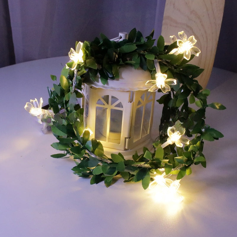 Soft cherry blossom LED fairy string light on a green leaf vine with a warm glow, decorative photo
