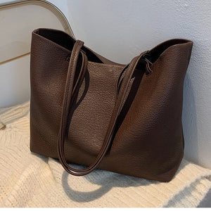 Dark brown PU leather tote bag with two long slim straps and a pebbled surface on a cream knit blanket