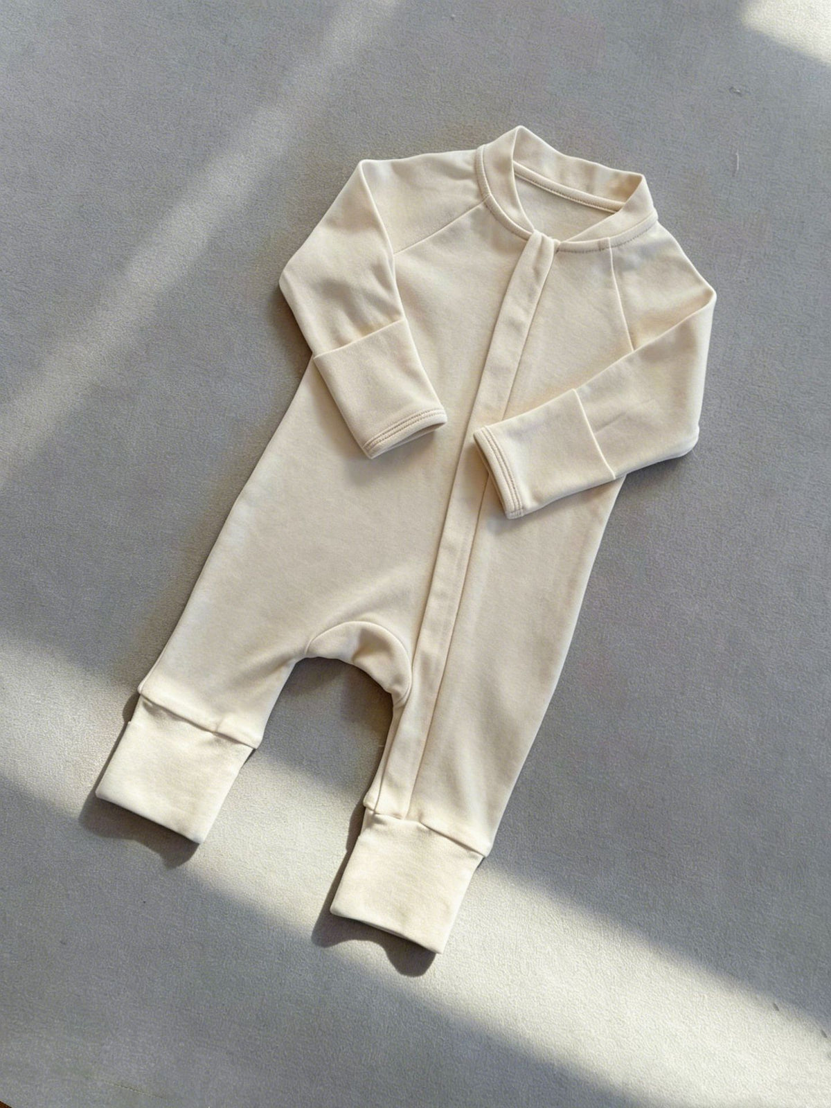 Cream zip front baby romper laid flat on a gray floor, image of the 80 cm, 12 to 18 months size option