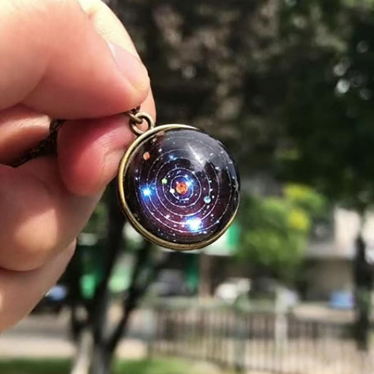 Hand holding the glass solar system pendant outdoors, sunlight through the dome and its printed orbits