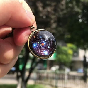 Hand holding the glass solar system pendant outdoors, sunlight through the dome and its printed orbits