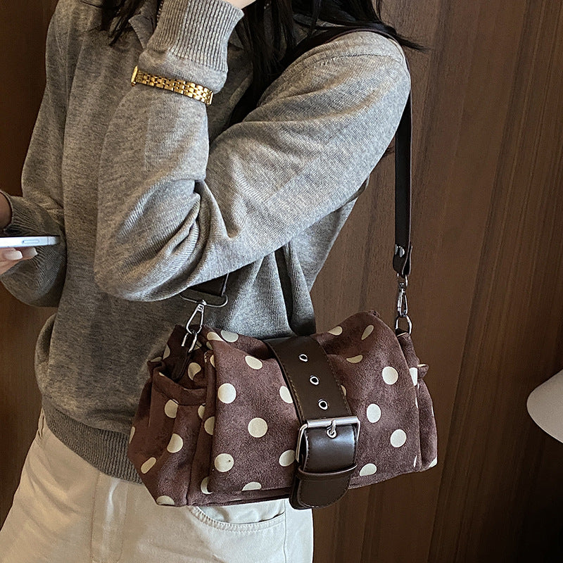 Side view of the brown polka dot shoulder bag with buckle band and side pocket worn over a gray sweater