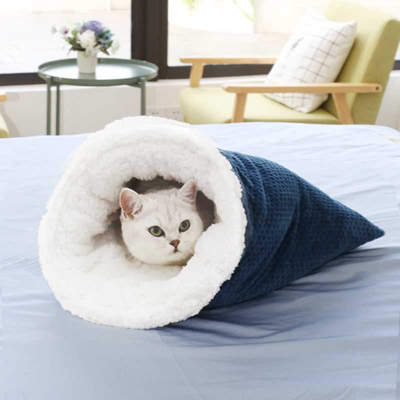Dark blue waffle weave cat sleeping bag with plush white fleece lining and a cat resting inside on a bed