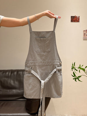 Front view of gray pinafore dress with square bib pocket and tie belt
