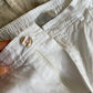 Close-up of white linen shorts mother-of-pearl button, zip fly and gathered waistband