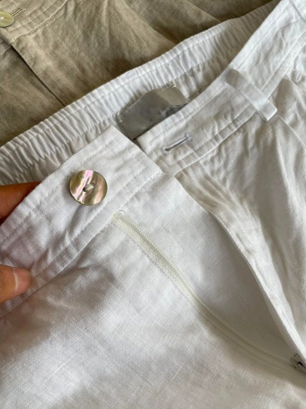 Close-up of white linen shorts mother-of-pearl button, zip fly and gathered waistband