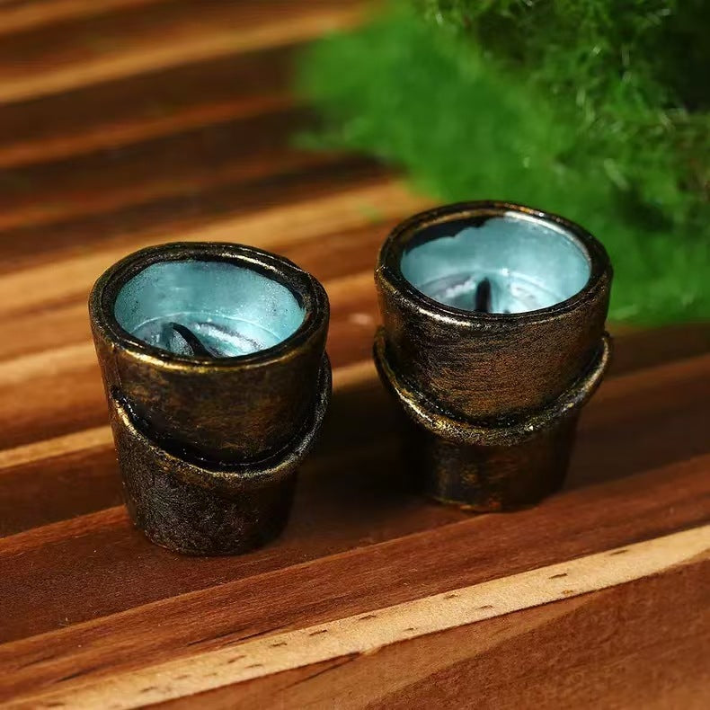 Two small gold toned resin fishing buckets with pale blue interiors on a wooden board