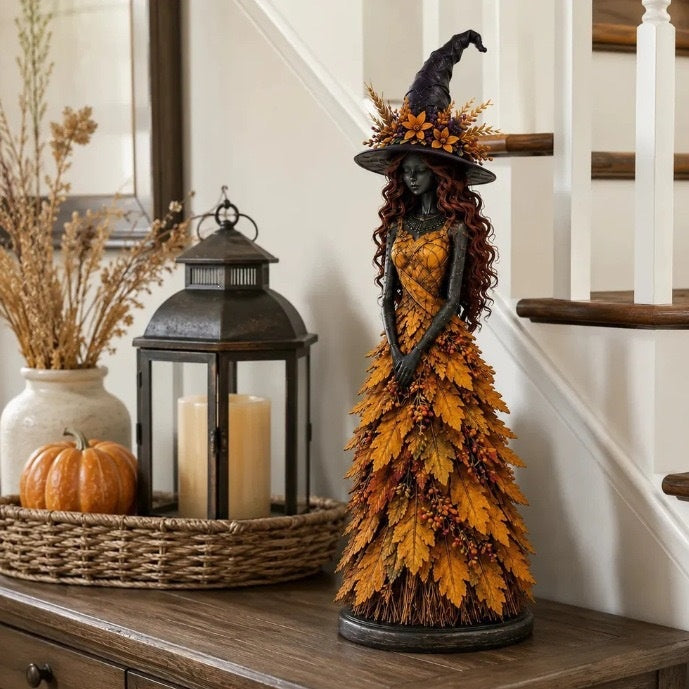 Witch statue in an orange leaf gown on a wooden console beside a lantern, candles and a pumpkin